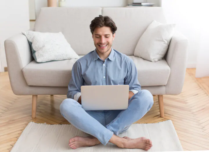 pria tersenyum duduk di lantai menggunakan laptop