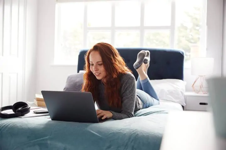 wanita menggunakan laptop di tempat tidur untuk belajar capm